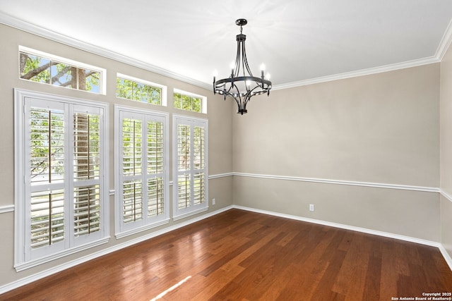 empty room with wood finished floors, a chandelier, ornamental molding, and baseboards