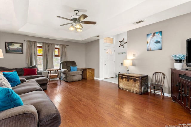 living area featuring wood finished floors, baseboards, visible vents, a raised ceiling, and a ceiling fan