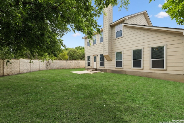 rear view of house with a chimney, a fenced backyard, a yard, and a patio area