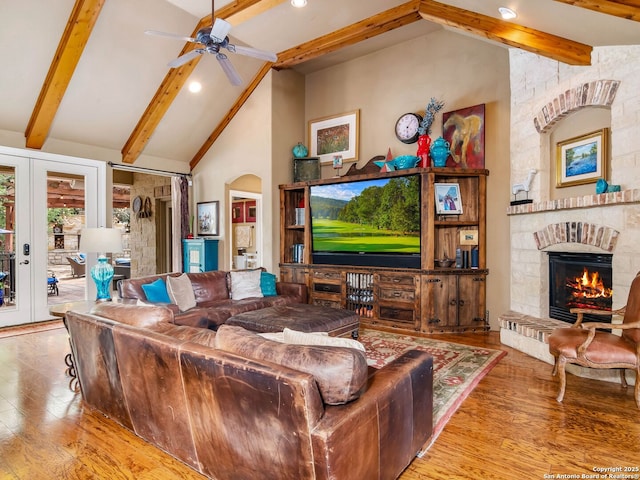 living area featuring vaulted ceiling with beams, ceiling fan, a stone fireplace, and wood finished floors
