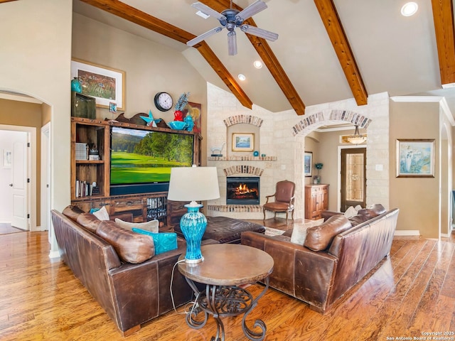 living area with arched walkways, a ceiling fan, beamed ceiling, and wood finished floors