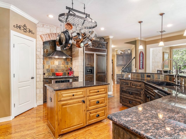 kitchen featuring a spacious island, wall chimney range hood, crown molding, and a sink