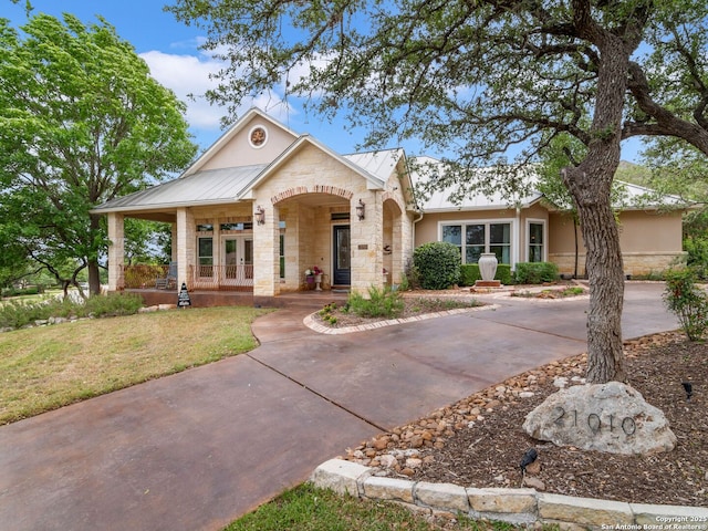 view of front of house with stone siding, a standing seam roof, metal roof, covered porch, and french doors