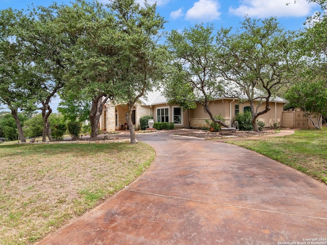 ranch-style home featuring stucco siding, fence, curved driveway, stone siding, and a front lawn