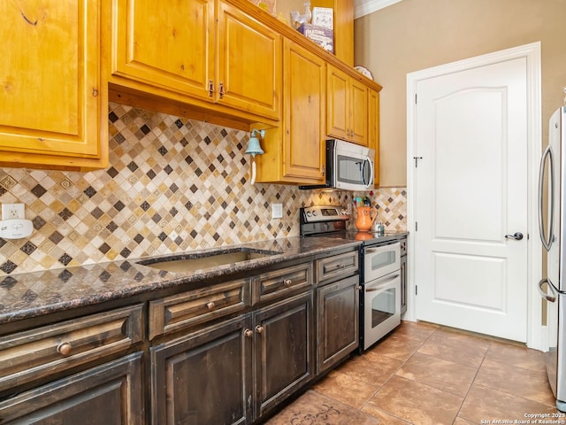 kitchen featuring dark stone counters, a sink, stainless steel appliances, and tasteful backsplash
