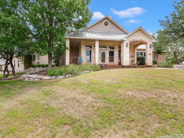 view of front of home featuring stone siding, a standing seam roof, metal roof, covered porch, and a front yard