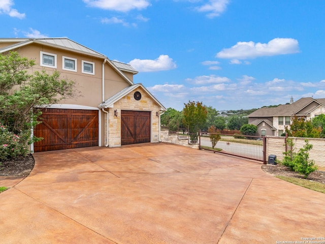 view of side of home with fence, stone siding, a gate, a standing seam roof, and stucco siding