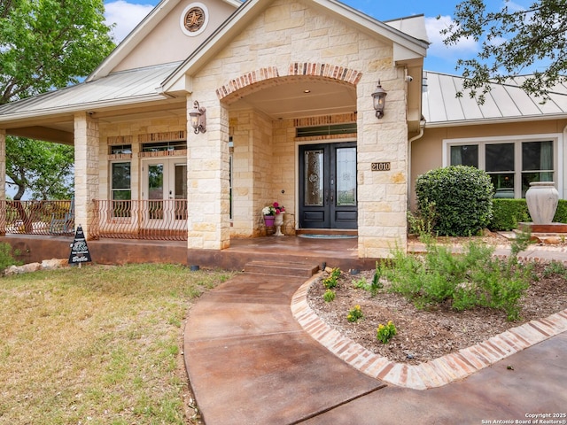 view of exterior entry with stone siding, a standing seam roof, metal roof, a porch, and french doors