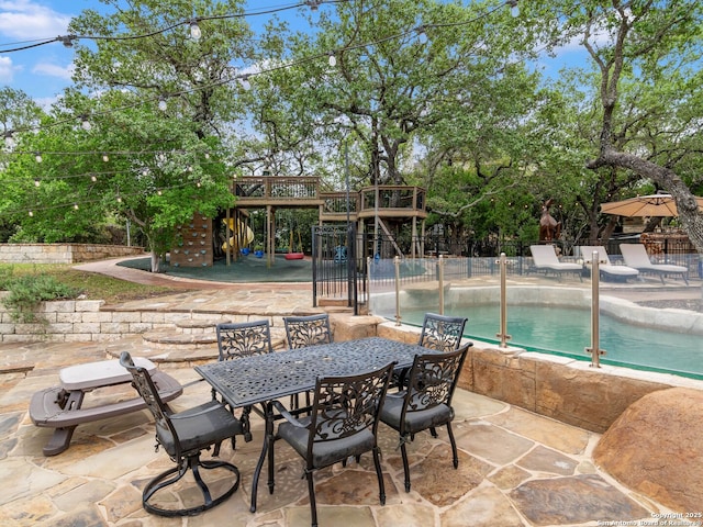 view of patio with fence, outdoor dining space, a playground, and an outdoor pool