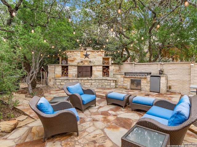 view of patio featuring fence, an outdoor living space with a fireplace, and exterior kitchen