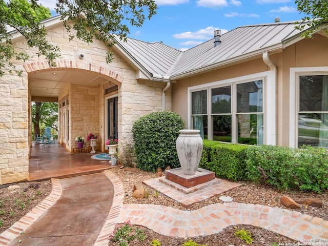 property entrance featuring metal roof, a standing seam roof, stone siding, and covered porch