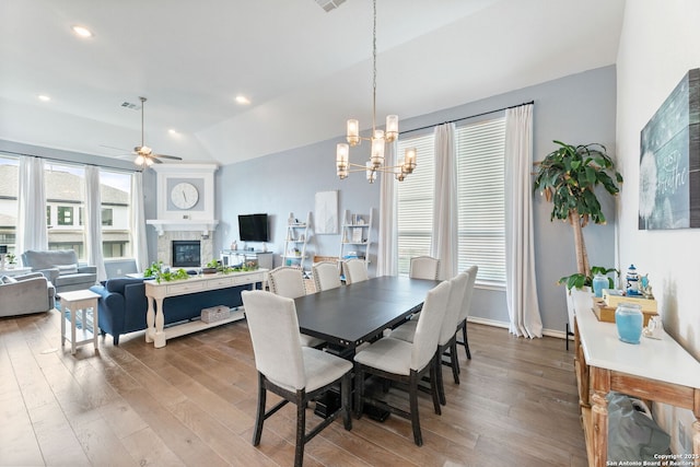 dining area featuring a wealth of natural light, wood finished floors, a tile fireplace, and ceiling fan with notable chandelier