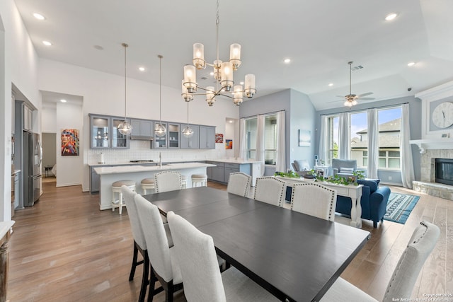 dining space featuring recessed lighting, ceiling fan with notable chandelier, light wood-style floors, and a stone fireplace