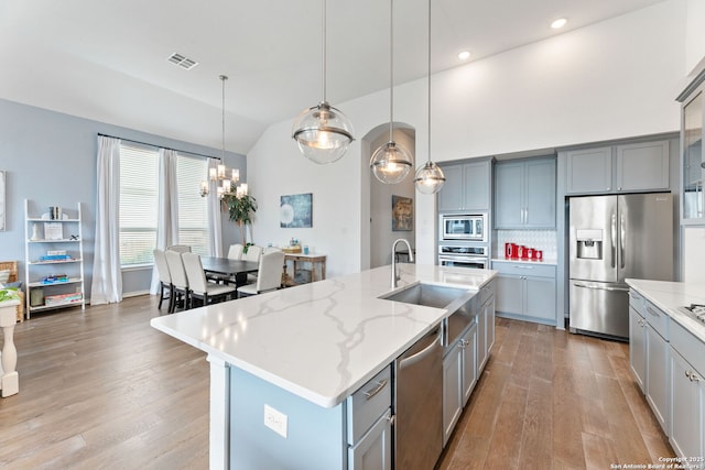 kitchen with a sink, stainless steel appliances, gray cabinets, hardwood / wood-style floors, and lofted ceiling