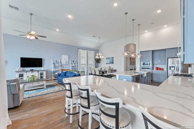 kitchen with appliances with stainless steel finishes, light wood-style floors, visible vents, light stone countertops, and ceiling fan with notable chandelier