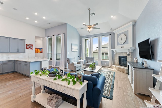 living area featuring light wood-style floors, visible vents, ceiling fan, and a stone fireplace