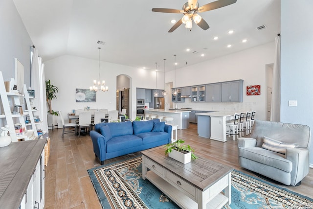 living room with light wood finished floors, visible vents, high vaulted ceiling, and ceiling fan with notable chandelier