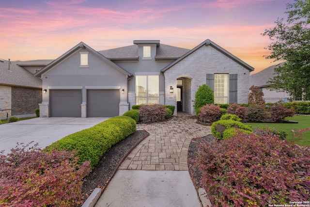traditional-style home featuring an attached garage, concrete driveway, stone siding, and stucco siding