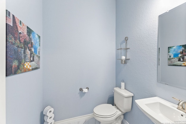 half bath featuring baseboards, toilet, and a sink