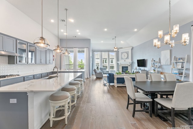 kitchen with hardwood / wood-style flooring, a sink, gray cabinets, stainless steel gas cooktop, and ceiling fan with notable chandelier