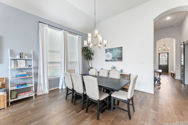 dining space featuring arched walkways, an inviting chandelier, hardwood / wood-style floors, visible vents, and lofted ceiling