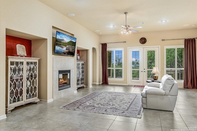 tiled living room featuring a tiled fireplace, baseboards, arched walkways, and ceiling fan