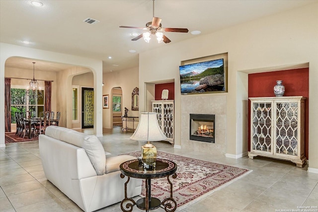 living room with visible vents, arched walkways, a tiled fireplace, tile patterned flooring, and ceiling fan with notable chandelier