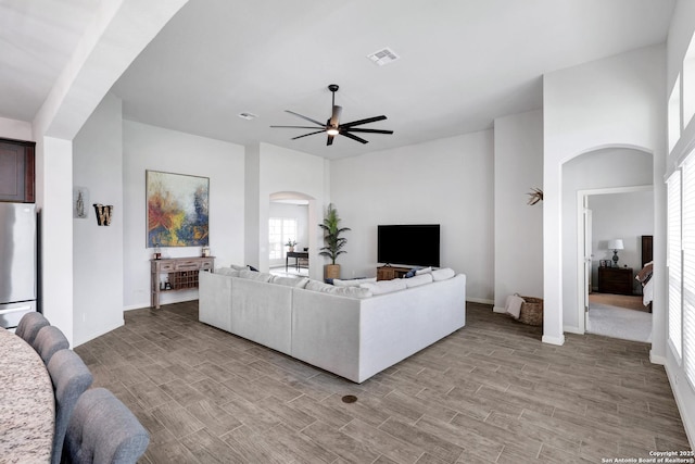 living area with visible vents, ceiling fan, baseboards, arched walkways, and light wood-type flooring