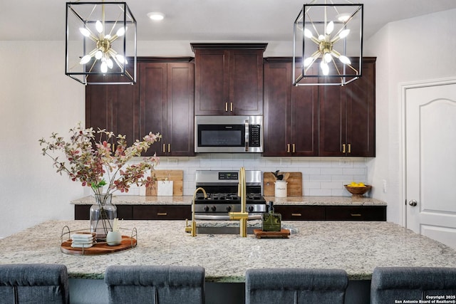 kitchen featuring a kitchen breakfast bar, a chandelier, stainless steel appliances, and decorative backsplash