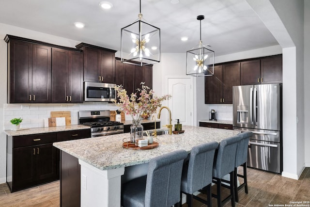 kitchen with decorative backsplash, appliances with stainless steel finishes, baseboards, light stone countertops, and a kitchen island with sink