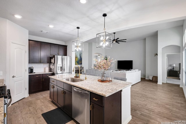 kitchen with a sink, stainless steel appliances, dark brown cabinetry, arched walkways, and light wood finished floors