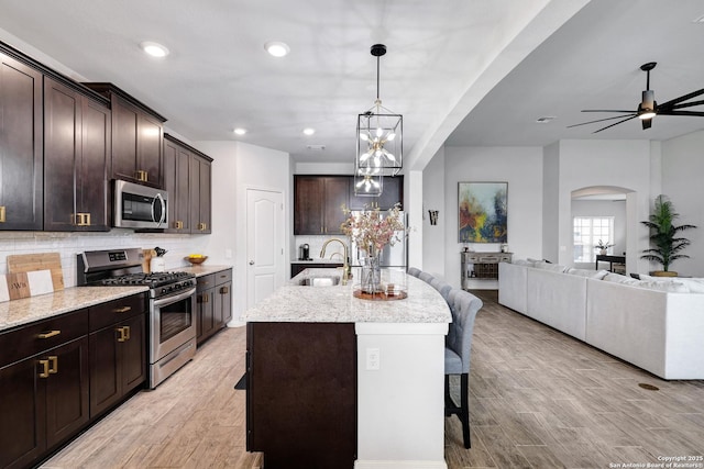 kitchen with arched walkways, appliances with stainless steel finishes, a sink, open floor plan, and a kitchen breakfast bar