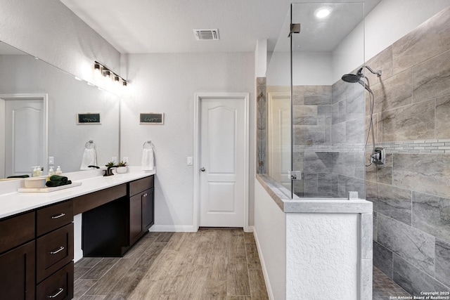 bathroom with vanity, a walk in shower, visible vents, baseboards, and wood finished floors