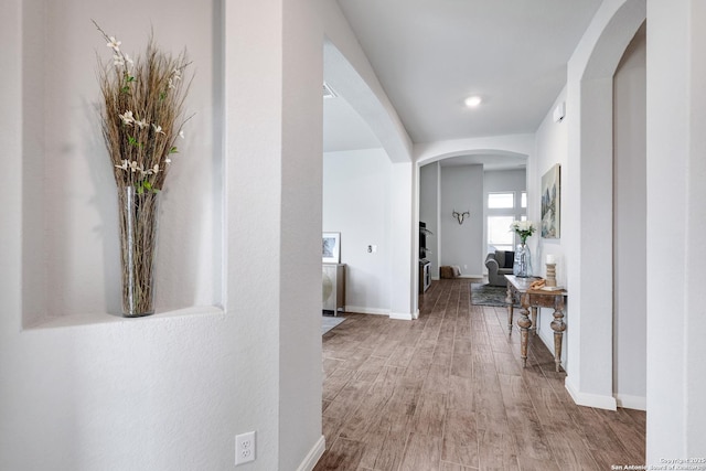 hall with baseboards, arched walkways, and wood finished floors