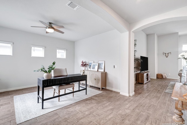 home office featuring light wood-style floors, visible vents, baseboards, arched walkways, and a ceiling fan