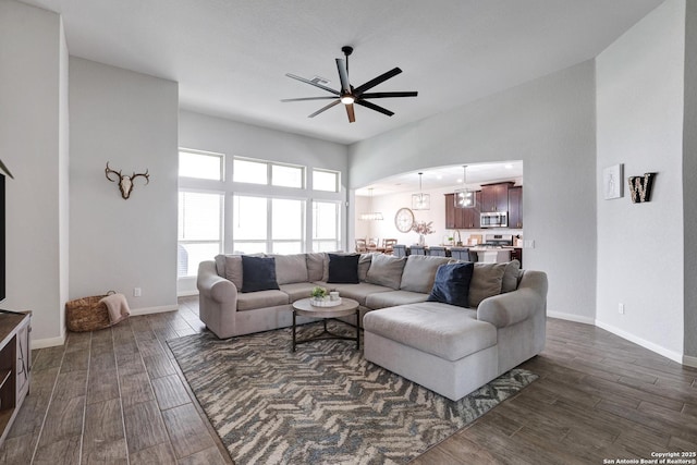 living area with a ceiling fan, baseboards, and dark wood-type flooring