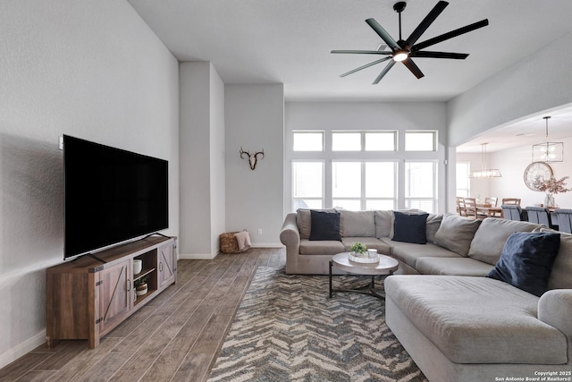 living area featuring baseboards, ceiling fan with notable chandelier, and light wood-style flooring