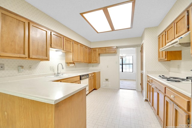 kitchen featuring a sink, under cabinet range hood, white dishwasher, a peninsula, and wallpapered walls
