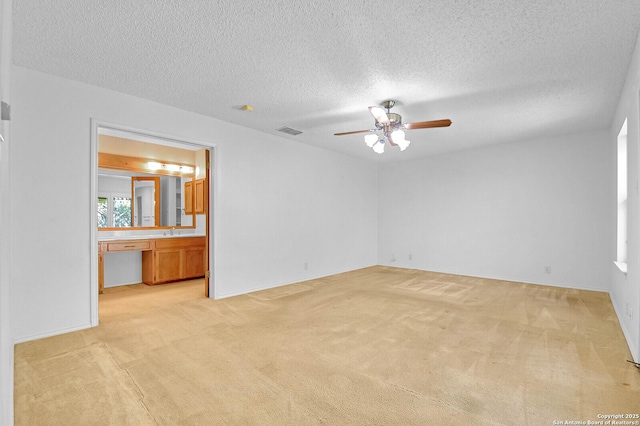 unfurnished room with a textured ceiling, visible vents, ceiling fan, and light colored carpet