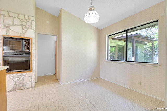 unfurnished room featuring a chandelier, wallpapered walls, vaulted ceiling, and baseboards