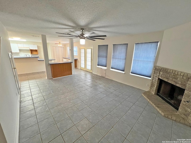 7514 Autumn Ledge, Converse, TX 78109 - unfurnished living room with a textured ceiling, ceiling fan, baseboards, a brick fireplace, and tile patterned floors