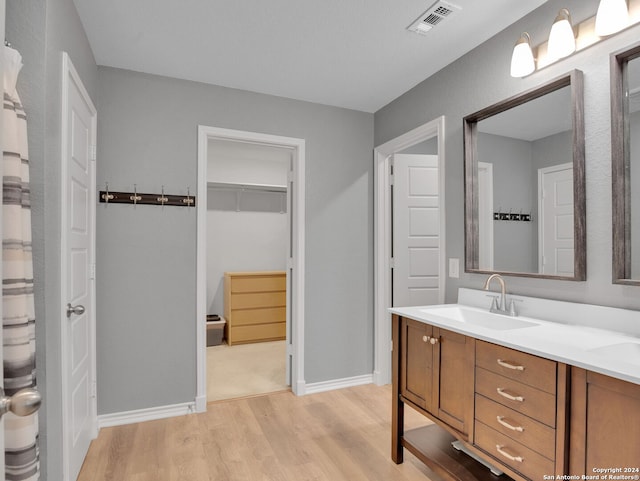 full bathroom featuring a sink, double vanity, visible vents, baseboards, and wood finished floors