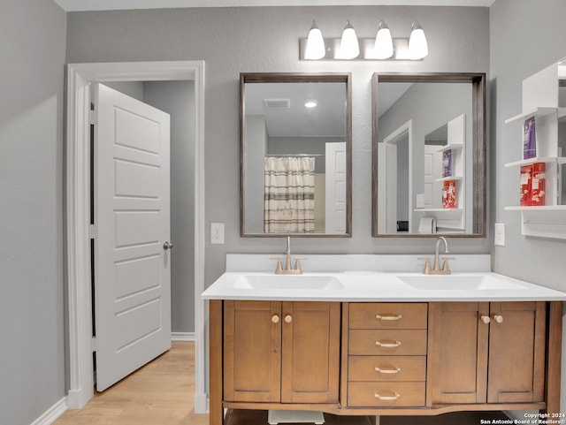 bathroom with visible vents, wood finished floors, double vanity, and a sink