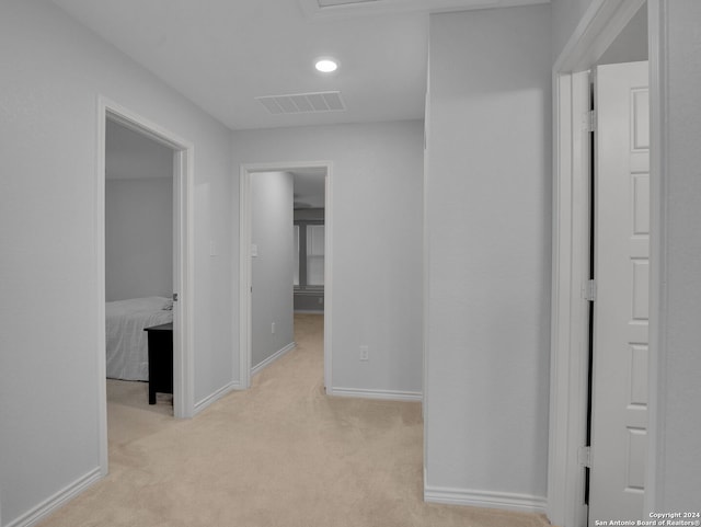 corridor with baseboards, visible vents, and light carpet
