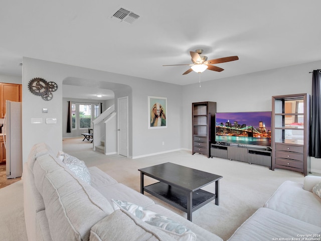 living area featuring ceiling fan, visible vents, baseboards, arched walkways, and light colored carpet