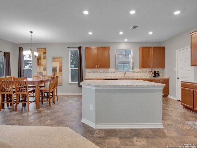 kitchen featuring light countertops, brown cabinets, a kitchen island, a sink, and a notable chandelier