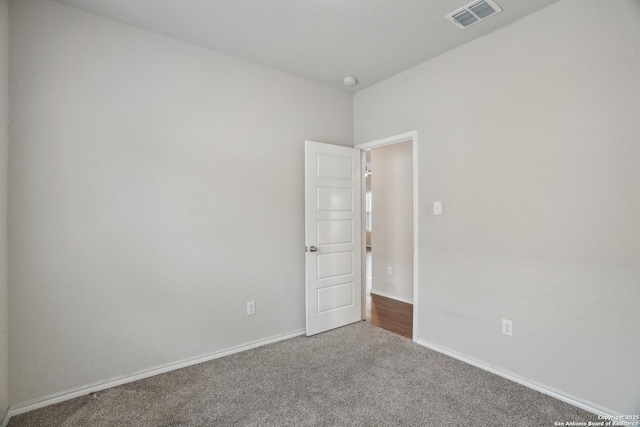 empty room with dark colored carpet, visible vents, and baseboards