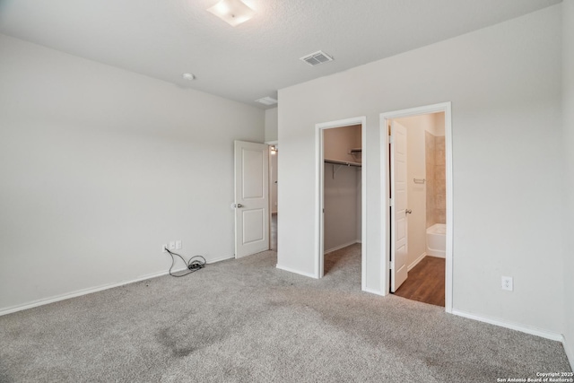 unfurnished bedroom featuring baseboards, a closet, carpet flooring, a walk in closet, and visible vents