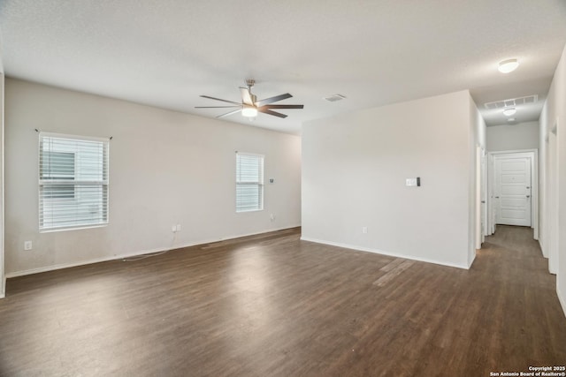 spare room with dark wood-style flooring, visible vents, a ceiling fan, and baseboards