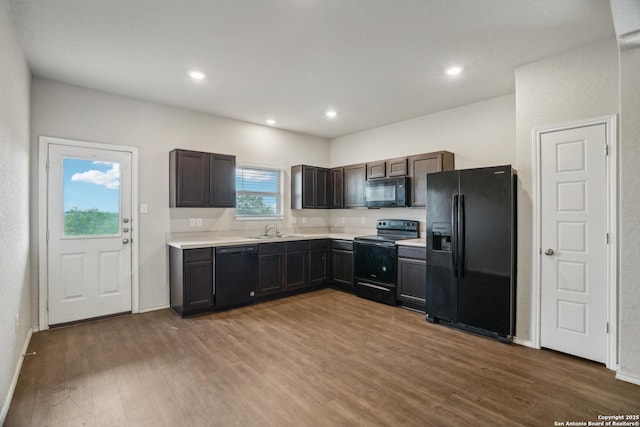 kitchen featuring black appliances, wood finished floors, light countertops, and a sink